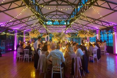 Miniature Location salle Fontains (Seine-et-Marne) - Château de Bourguignon #32 Vue nocturne d'une verrière illuminée par des lumières violettes, entourée d'arbres et d'un jardin.