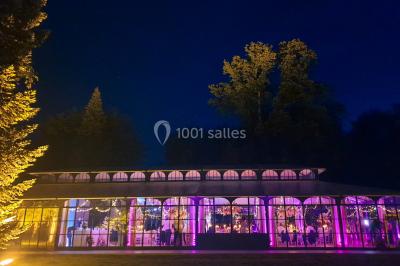 Miniature Location salle Fontains (Seine-et-Marne) - Château de Bourguignon #33 Vue nocturne d'une verrière illuminée par des lumières violettes, entourée d'arbres et d'un jardin.