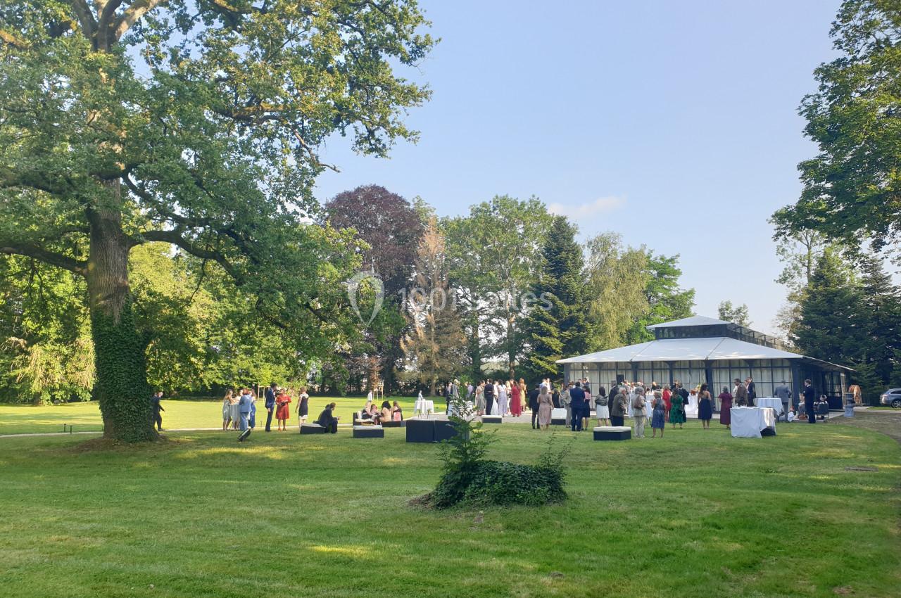 Location salle Fontains (Seine-et-Marne) - Château de Bourguignon #2 Groupe de personnes rassemblées près d'un bâtiment vitré dans un parc verdoyant par une journée ensoleillée.