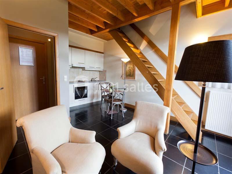 Intérieur d'un duplex avec salon, cuisine équipée, table à manger, escalier en bois et éclairage chaleureux.
