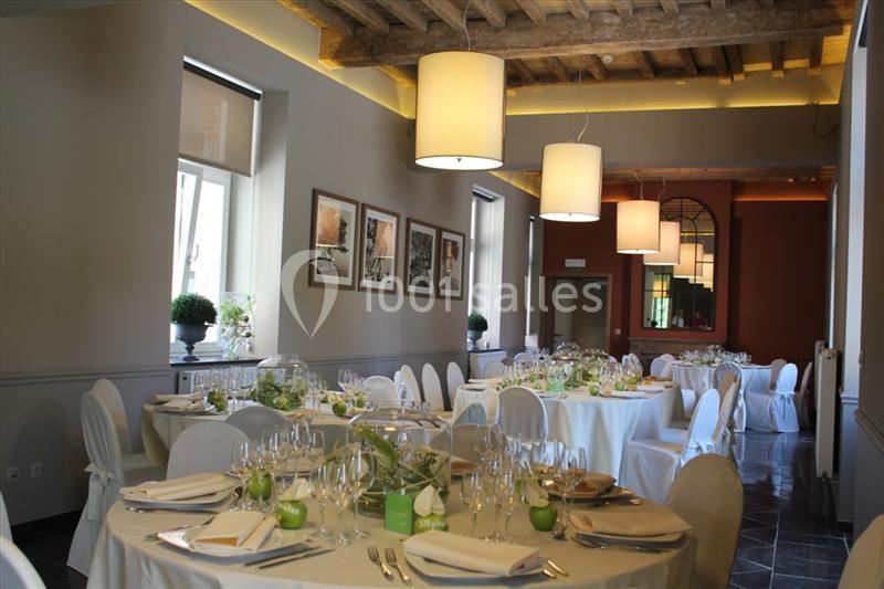 Salle de réception élégante avec tables dressées, nappes blanches, décorations florales et lumière naturelle.