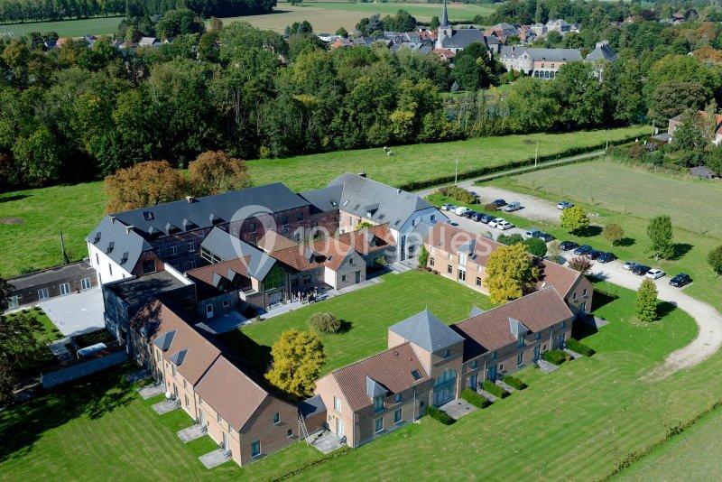 Vue aérienne d'un ensemble de bâtiments en briques entouré de verdure, avec un village en arrière-plan.