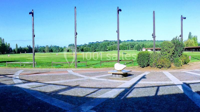 Vue d'un terrain de golf avec des cibles à l'arrière-plan, entouré de végétation et éclairé par un ciel dégagé.