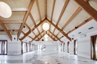 Salle de réception décorée avec des tables rondes, nappes blanches et chaises ornées de nœuds colorés.