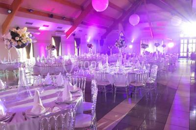 Salle de réception décorée avec des tables rondes, nappes blanches et chaises ornées de nœuds colorés.