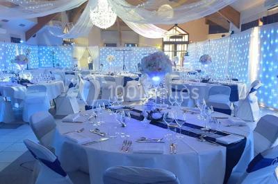 Salle de réception décorée avec des tables rondes, nappes blanches et chaises ornées de nœuds colorés.