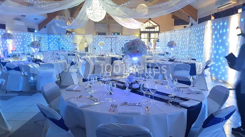 Salle de réception décorée avec des tables rondes dressées, éclairage bleu et blanc, et un lustre central.