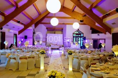 Salle de réception décorée avec des tables rondes, nappes blanches et chaises ornées de nœuds colorés.
