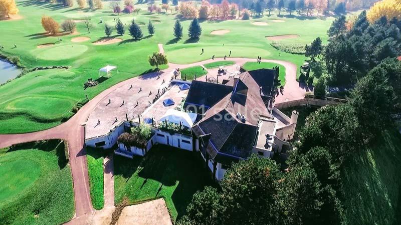Vue aérienne d'un club de golf entouré de pelouses, d'arbres et de terrains avec bunkers et obstacles.