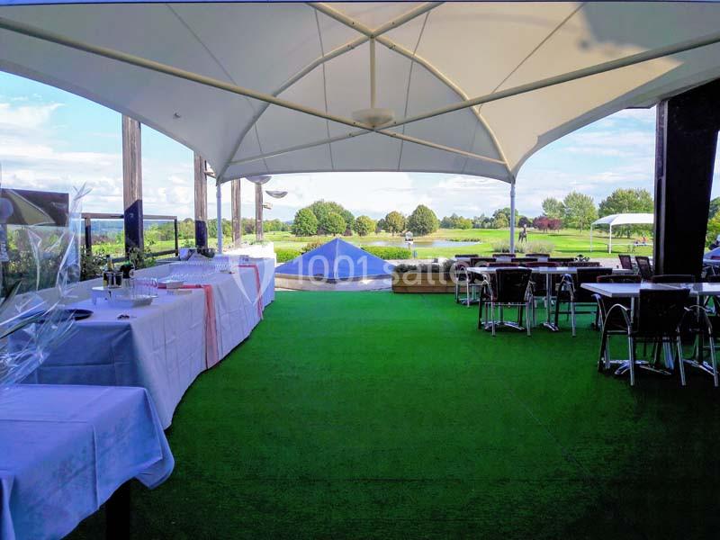 Terrasse couverte avec tables dressées, vue sur un espace vert et ciel dégagé en arrière-plan.