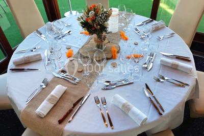 Salle de réception décorée avec des tables rondes, nappes blanches et chaises ornées de nœuds colorés.