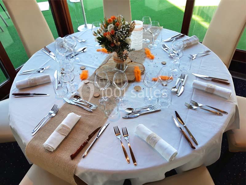 Table ronde élégamment dressée avec nappe blanche, couverts, verres, serviettes et centre de table floral.