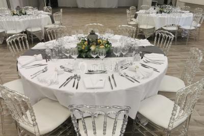 Salle de réception décorée avec des tables rondes, nappes blanches et chaises ornées de nœuds colorés.