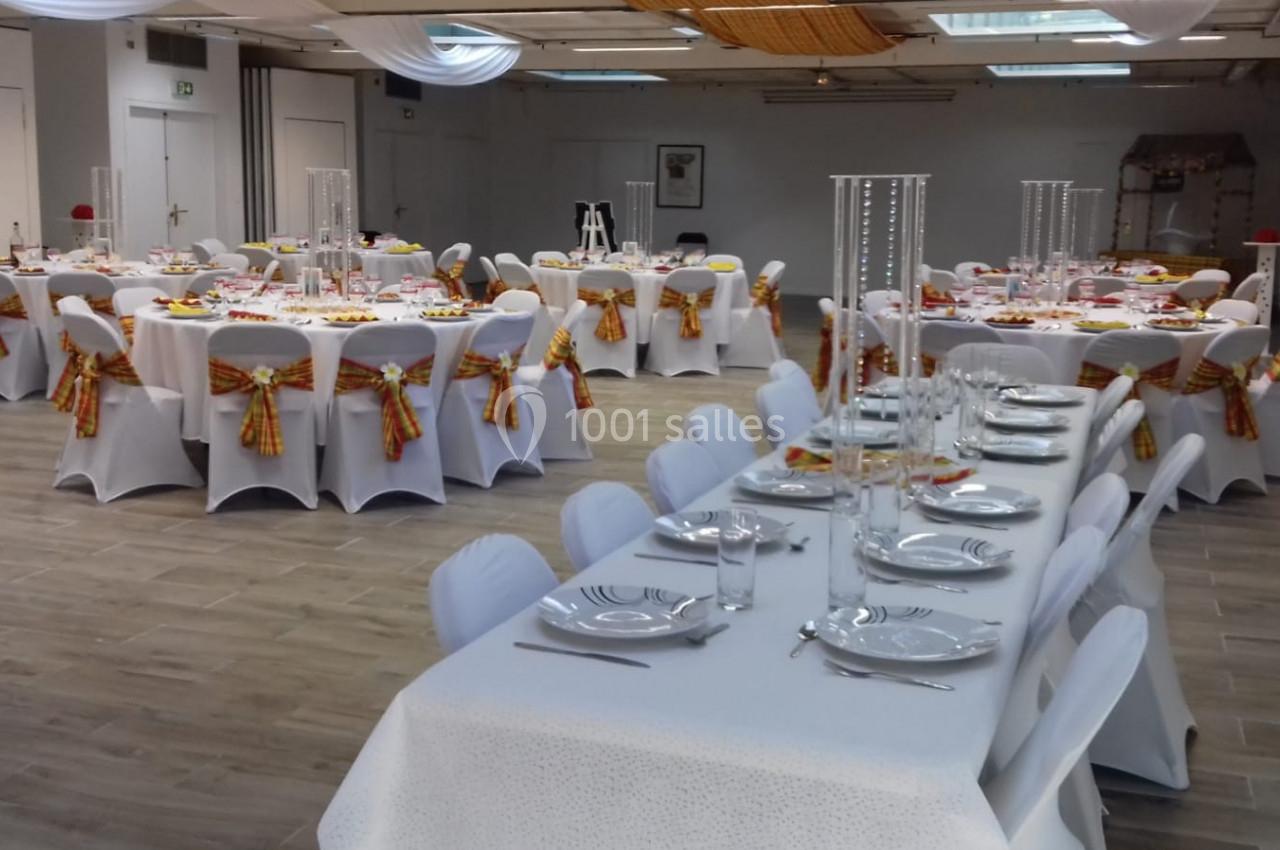 Salle de réception décorée avec des tables dressées, nappes blanches et chaises ornées de nœuds colorés.