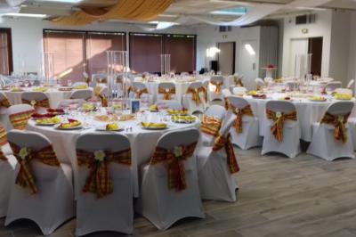 Salle de réception décorée avec des tables rondes, nappes blanches et chaises ornées de nœuds colorés.