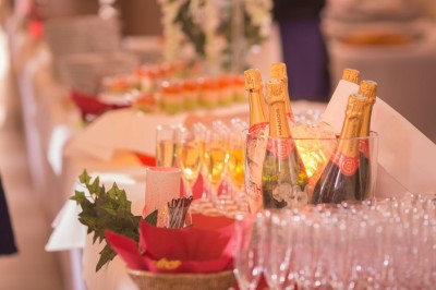 Salle lumineuse avec tables rondes dressées, nappes blanches, chaises rouges et décorations florales élégantes.
