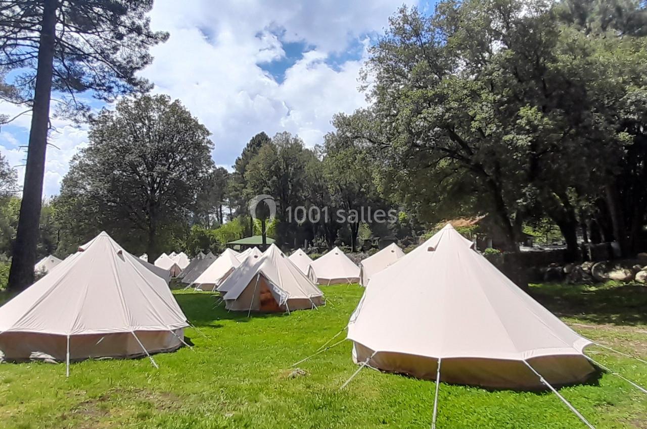 Tentes blanches installées sur une pelouse entourée d'arbres sous un ciel partiellement nuageux.