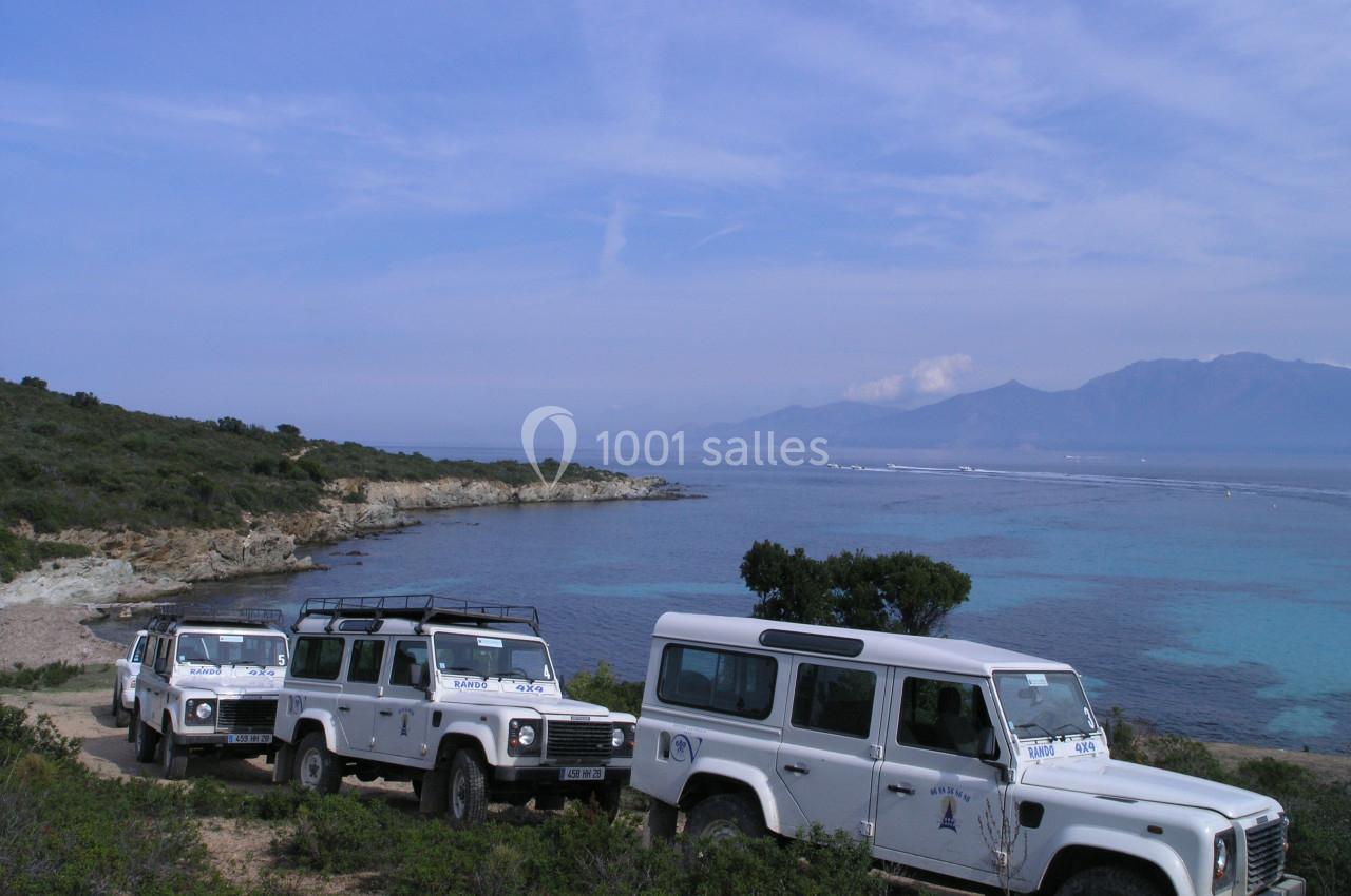 Quatre véhicules tout-terrain blancs stationnés sur un chemin côtier avec vue sur la mer et des collines à l'horizon.