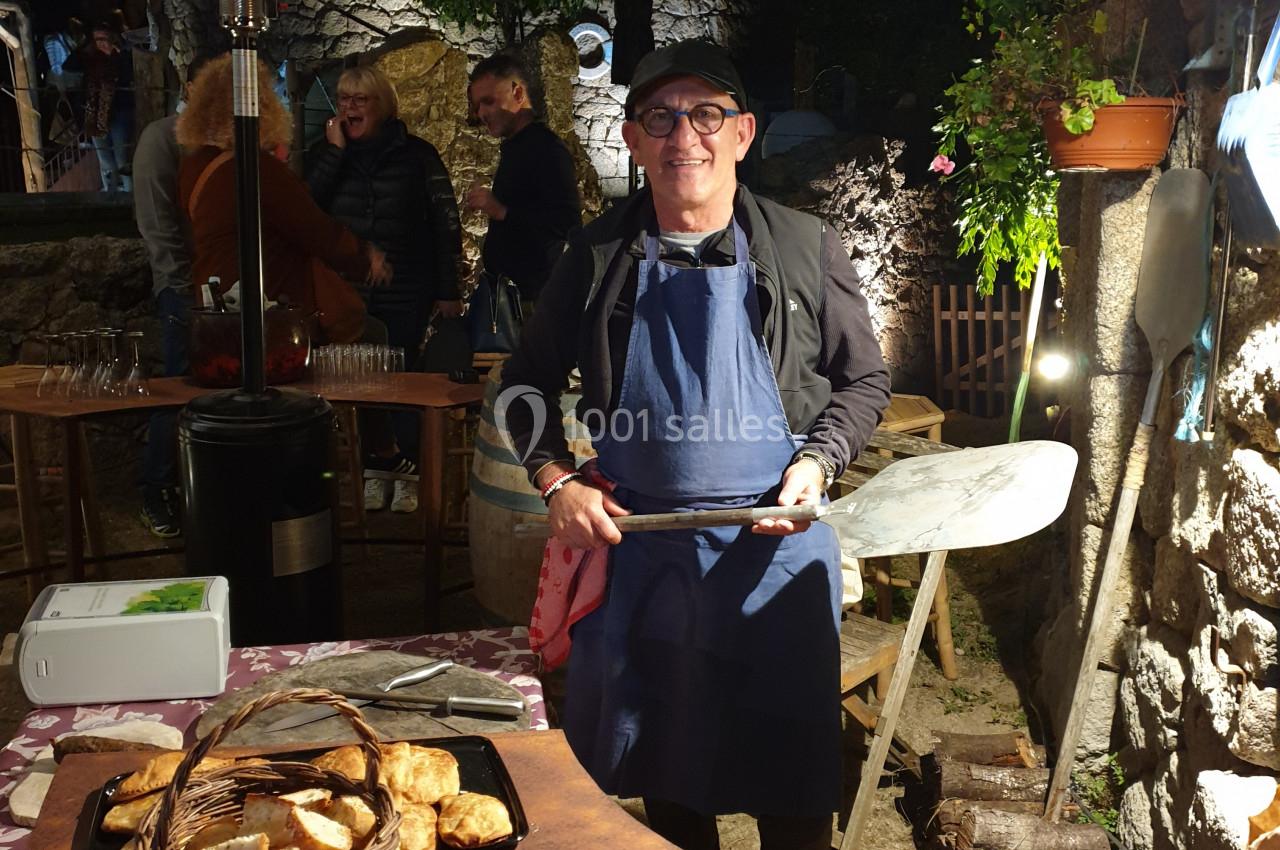 Un homme en tablier sert des plats cuisinés lors d'un événement en plein air, éclairé par une lampe chauffante.