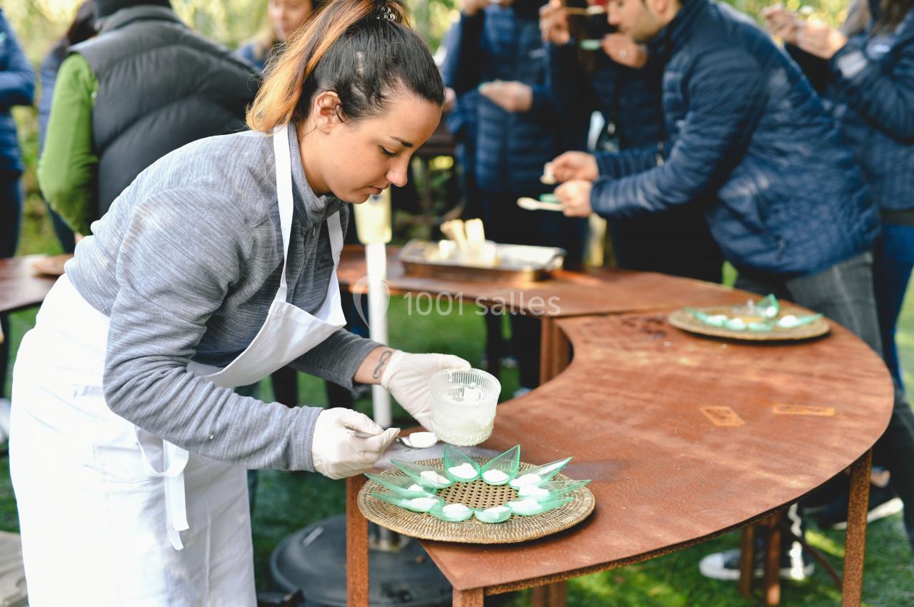 Une femme en tablier prépare un plat décoratif sur une table en extérieur lors d'un événement culinaire.