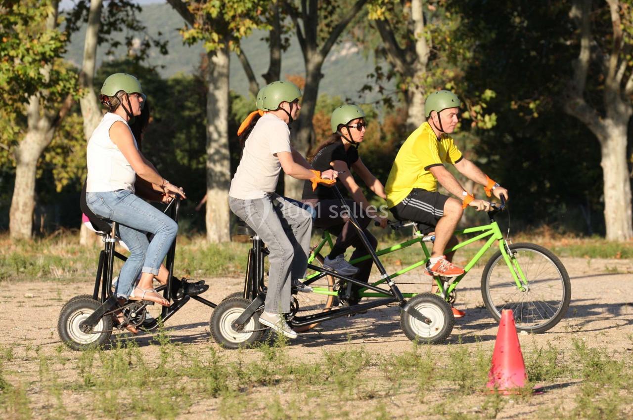 Quatre personnes portant des casques roulent en tandem sur des vélos dans un espace extérieur ensoleillé.