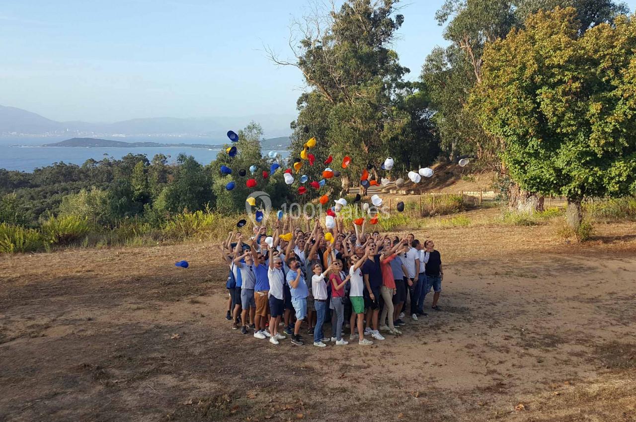 Un groupe de personnes en cercle lance des chapeaux colorés en l'air dans un paysage naturel.