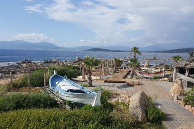 Barques traditionnelles sur une plage bordée de végétation, avec vue sur la mer et des montagnes à l'horizon.