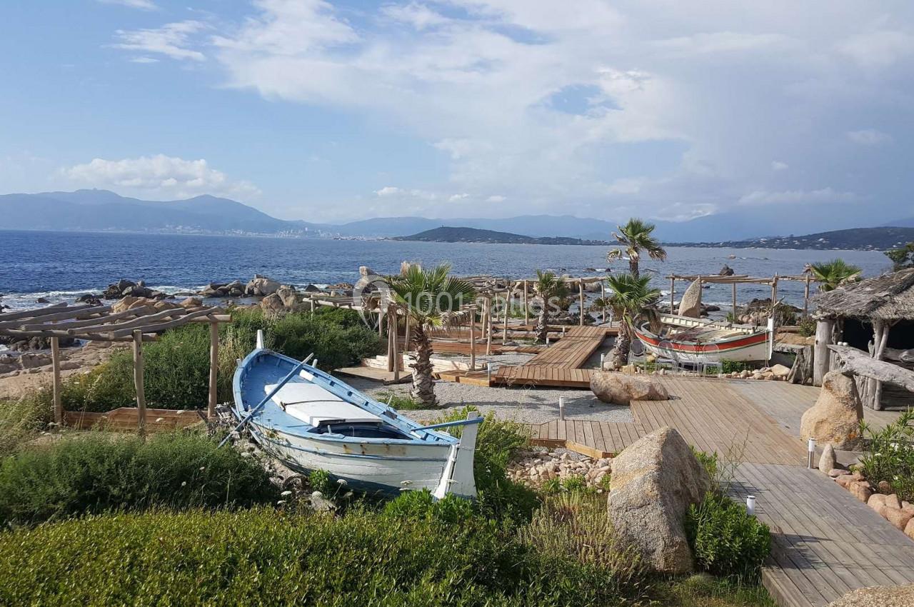 Barques traditionnelles sur une plage bordée de végétation, avec vue sur la mer et des montagnes à l'horizon.