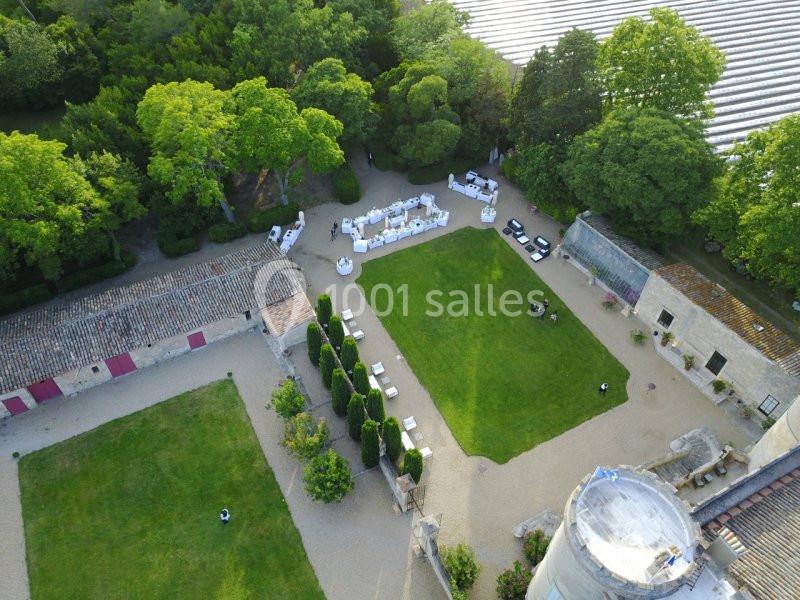 Vue aérienne d'une cour de château avec pelouse centrale, tables dressées, bâtiments anciens et arbres environnants.