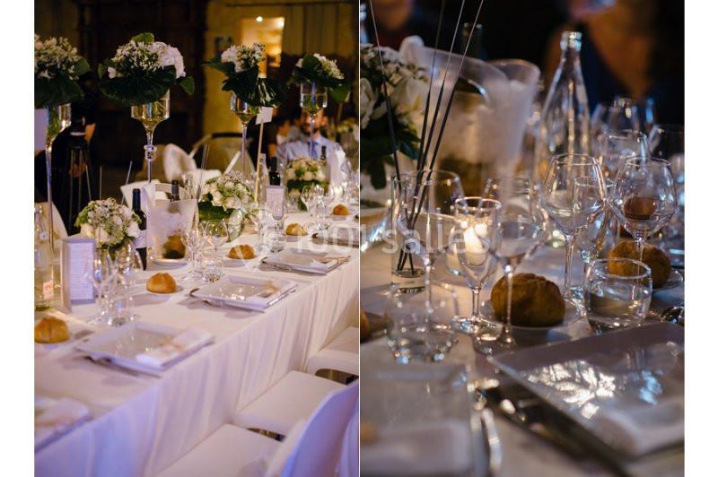 Table de réception élégamment dressée avec nappes blanches, fleurs, verres, assiettes et petits pains disposés.