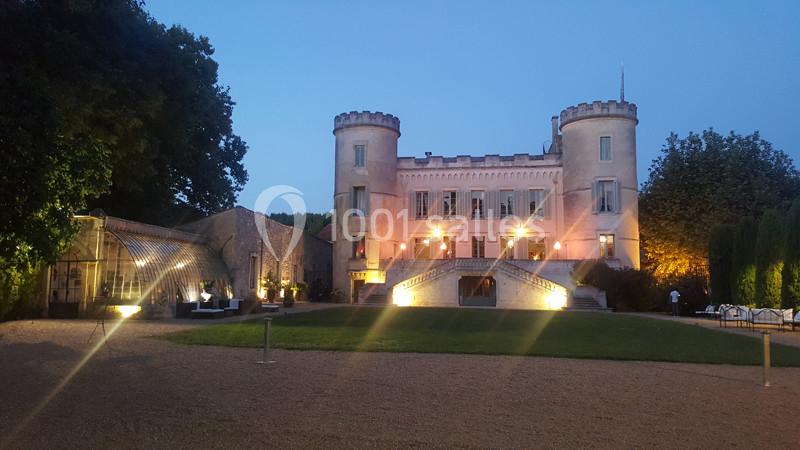 Façade éclairée d'un château avec deux tours, entouré d'arbres, vue depuis une cour au crépuscule.