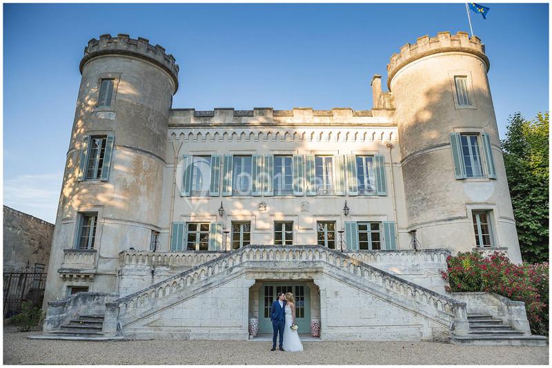 Un couple en tenue de mariage pose devant un château avec deux tours et un escalier central en pierre.