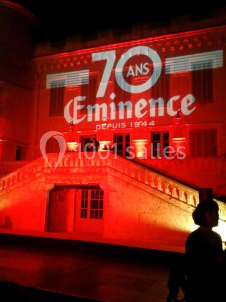 Projection lumineuse ’70 ans Eminence depuis 1944’ sur la façade d'un bâtiment éclairé en rouge, avec un escalier central.