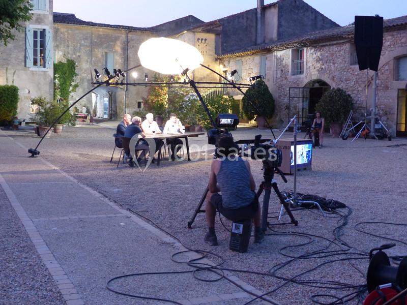 Tournage en extérieur dans une cour pavée, avec une équipe filmant un groupe assis sous un éclairage artificiel.