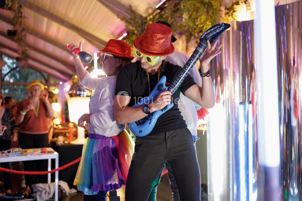 Deux personnes déguisées dansent et miment de jouer de la musique lors d'une fête dans un espace décoré.