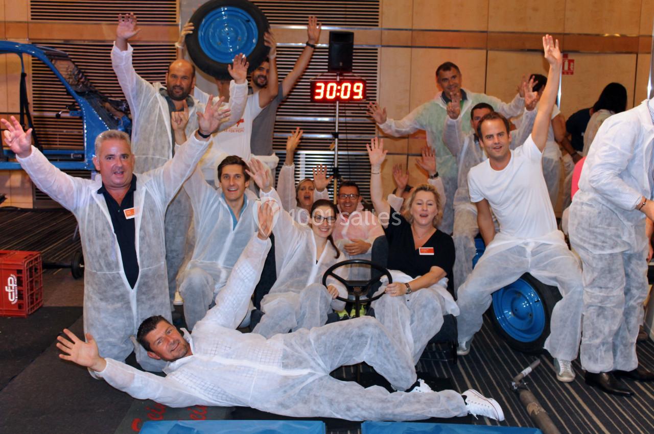 Un groupe de personnes en combinaisons blanches pose joyeusement devant un chronomètre dans un cadre intérieur.