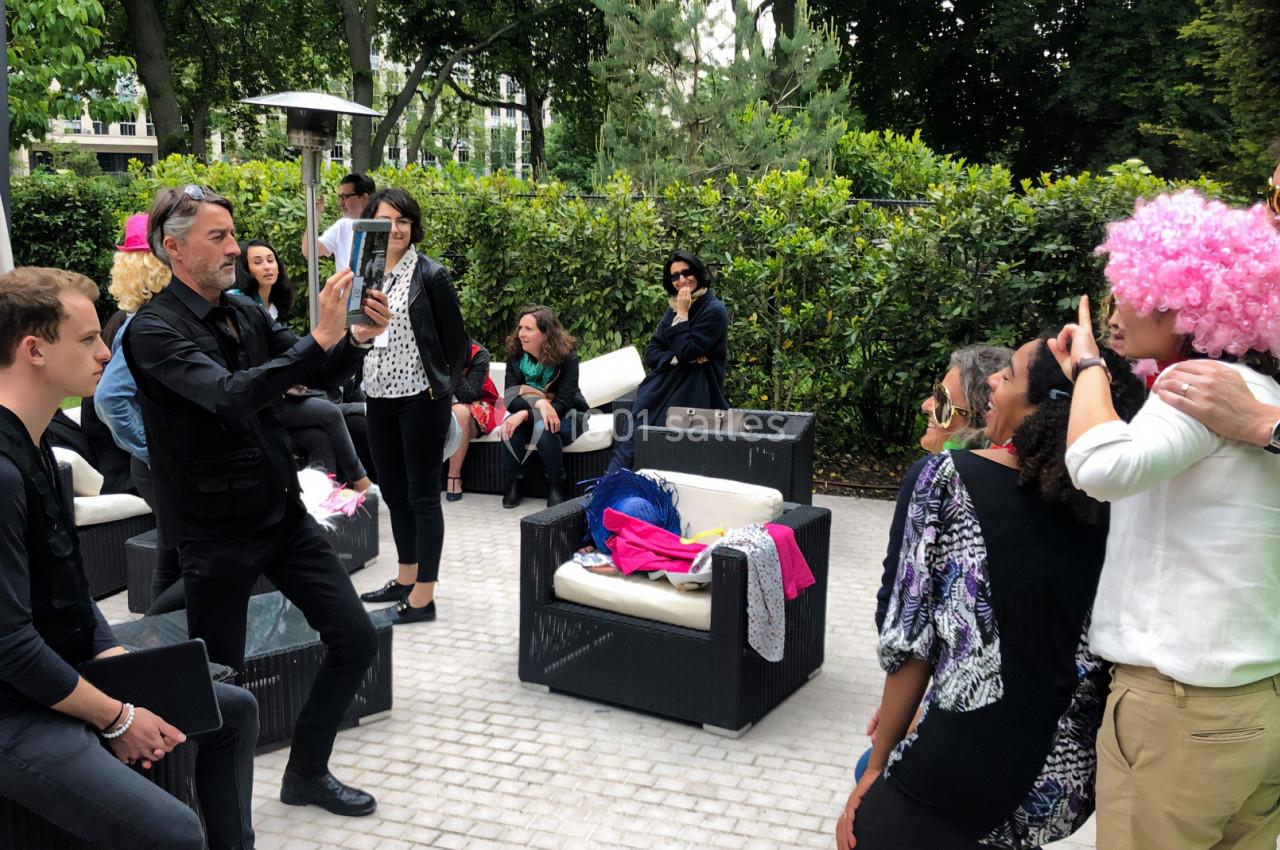 Un groupe de personnes dans un jardin, certaines déguisées, posant pour une photo prise par un homme avec une tablette.
