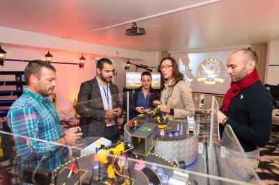 Des personnes debout en cercle dans une grande salle colorée, participant à une activité collective.