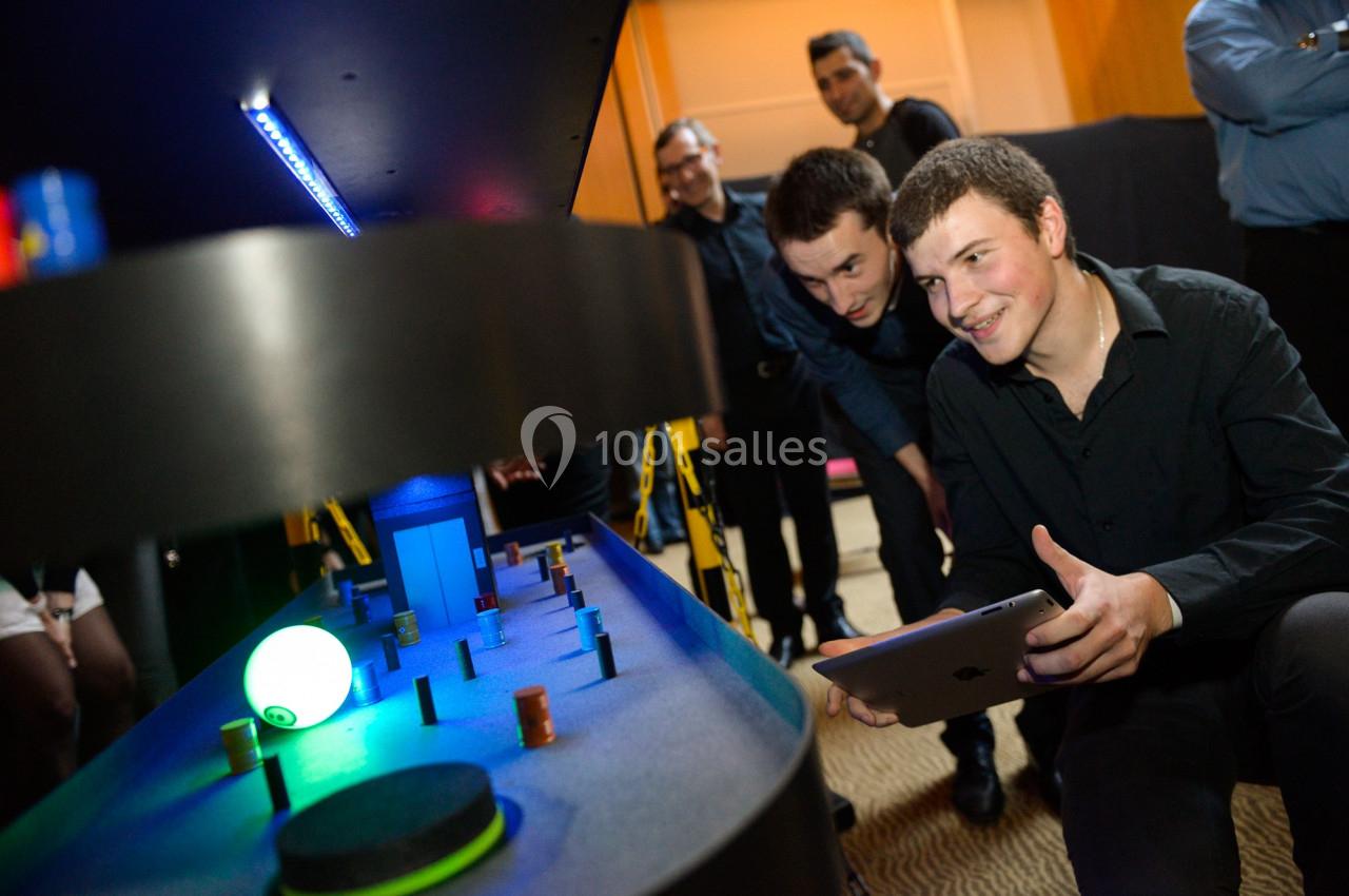 Deux hommes interagissent avec un jeu interactif lumineux sur une table dans un environnement intérieur.