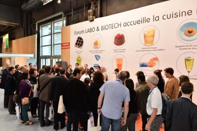 Des personnes debout en cercle dans une grande salle colorée, participant à une activité collective.