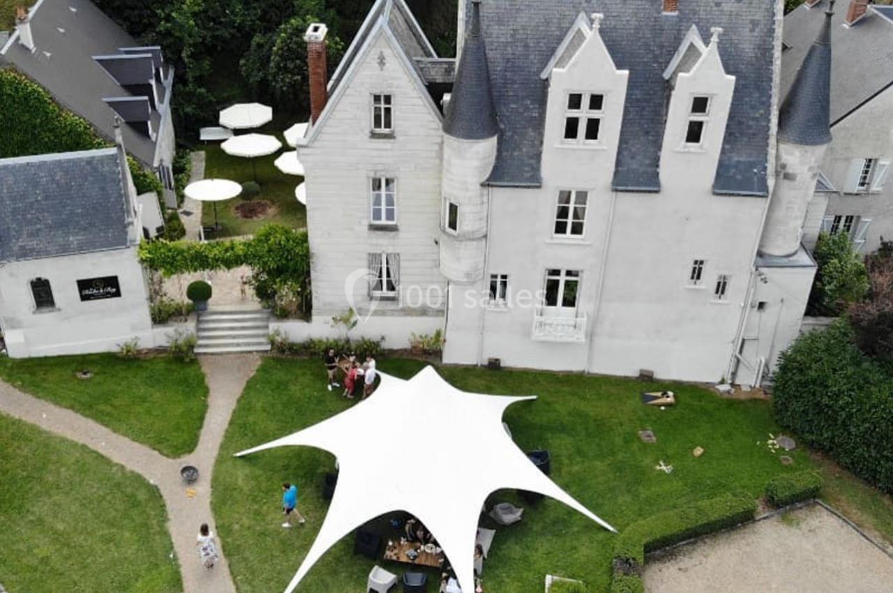 Vue aérienne d'un manoir blanc avec une grande tente blanche dans le jardin, entouré de verdure et de chemins.