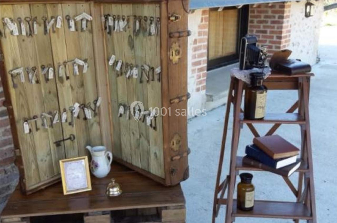 Armoire en bois ouverte avec des clés suspendues, à côté d'une échelle portant des livres et des objets anciens.