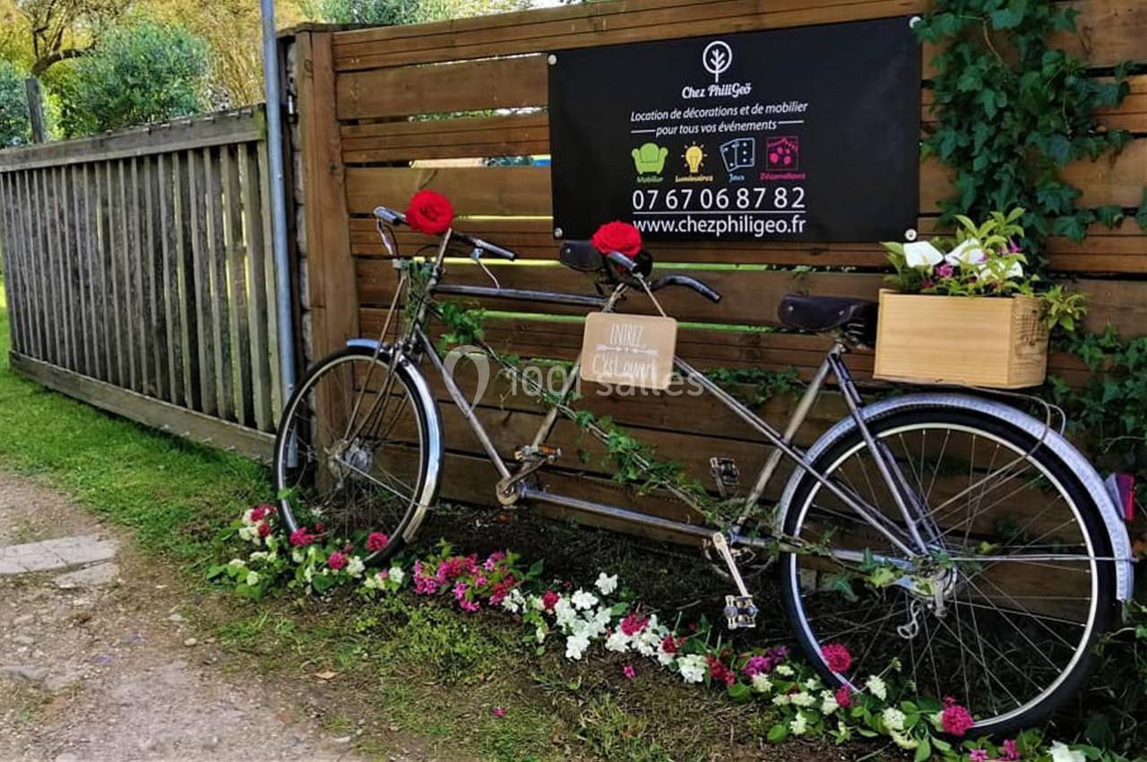 Un tandem décoré de fleurs et d'une caisse en bois, appuyé contre une clôture en bois avec un panneau publicitaire.