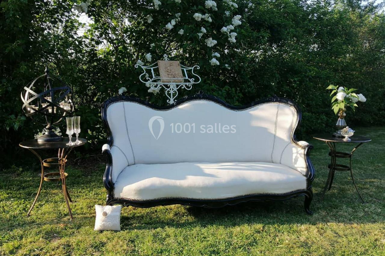 Canapé blanc ancien avec structure noire, entouré de petites tables décoratives, disposé sur une pelouse verdoyante.