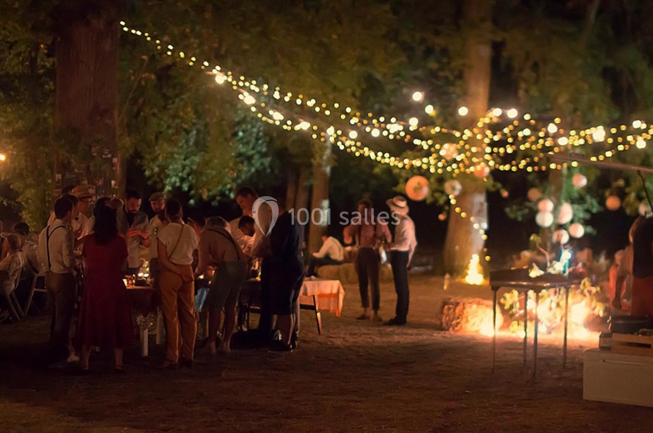 Groupe de personnes réunies en soirée dans un jardin éclairé par des guirlandes lumineuses suspendues aux arbres.