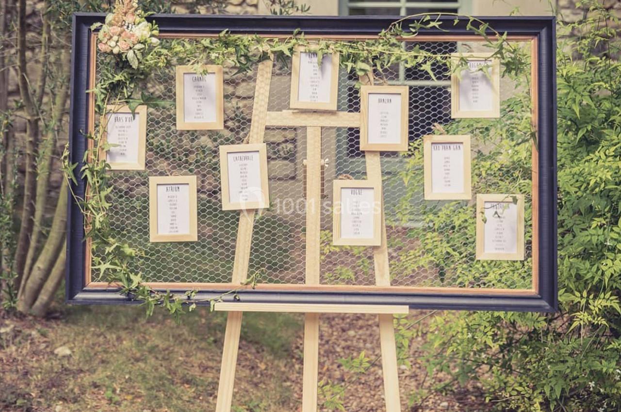 Tableau de plan de table de mariage avec cadres suspendus sur un grillage décoré de feuillage et de fleurs.