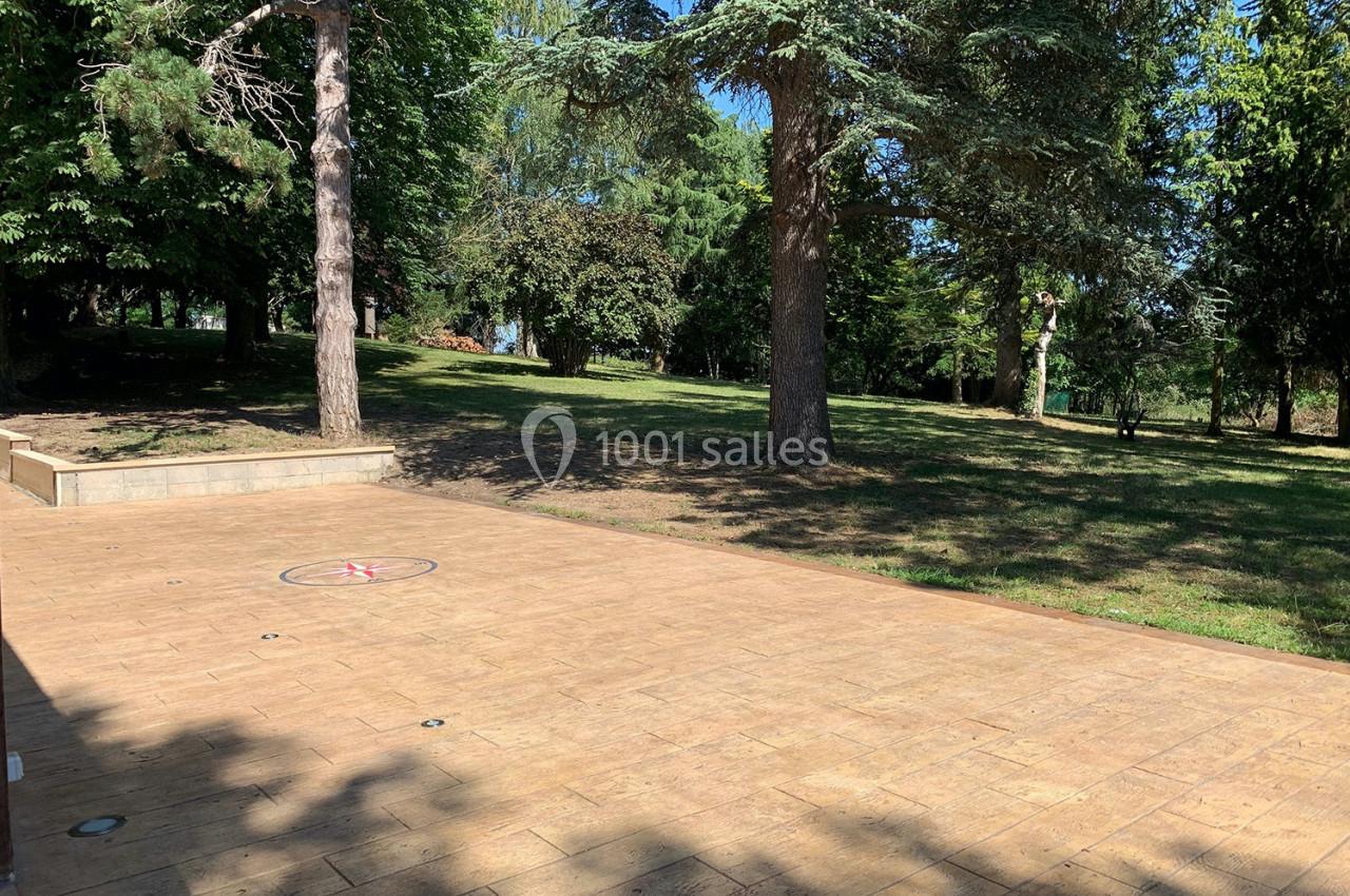 Terrasse en bois clair donnant sur un parc arboré avec pelouse et arbres sous un ciel dégagé.