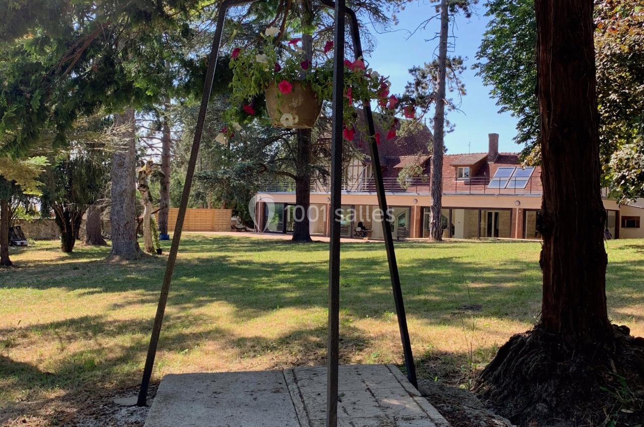 Un puits en pierre surmonté d'une structure métallique avec un pot de fleurs, entouré d'arbres dans un jardin.