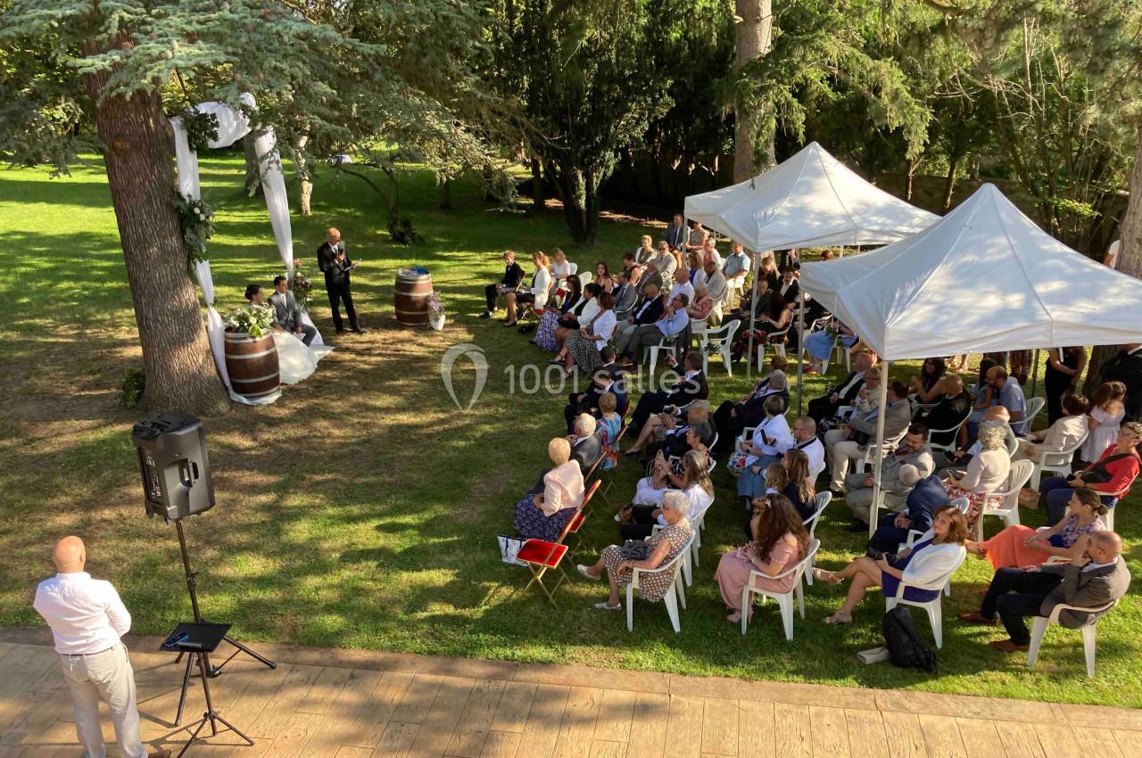 Cérémonie en plein air avec des invités assis sous des arbres et des tentes blanches dans un cadre verdoyant.
