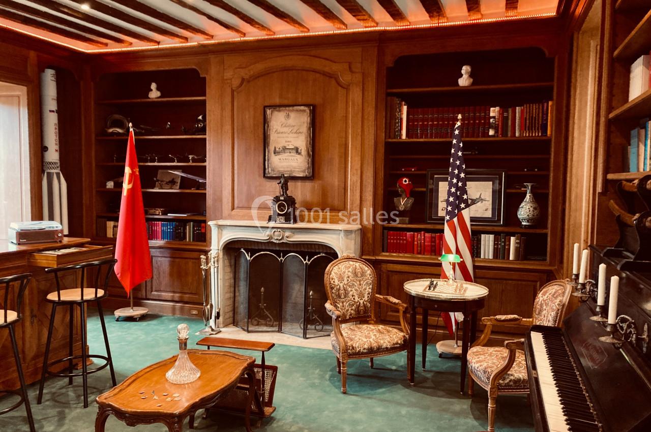 Bibliothèque avec cheminée, drapeaux chinois et américain, piano, fauteuils anciens et étagères remplies de livres.